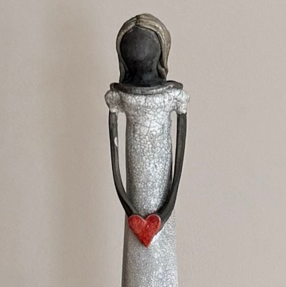 Close up of the top half of a black clay lady statue with a red heart on a plain background