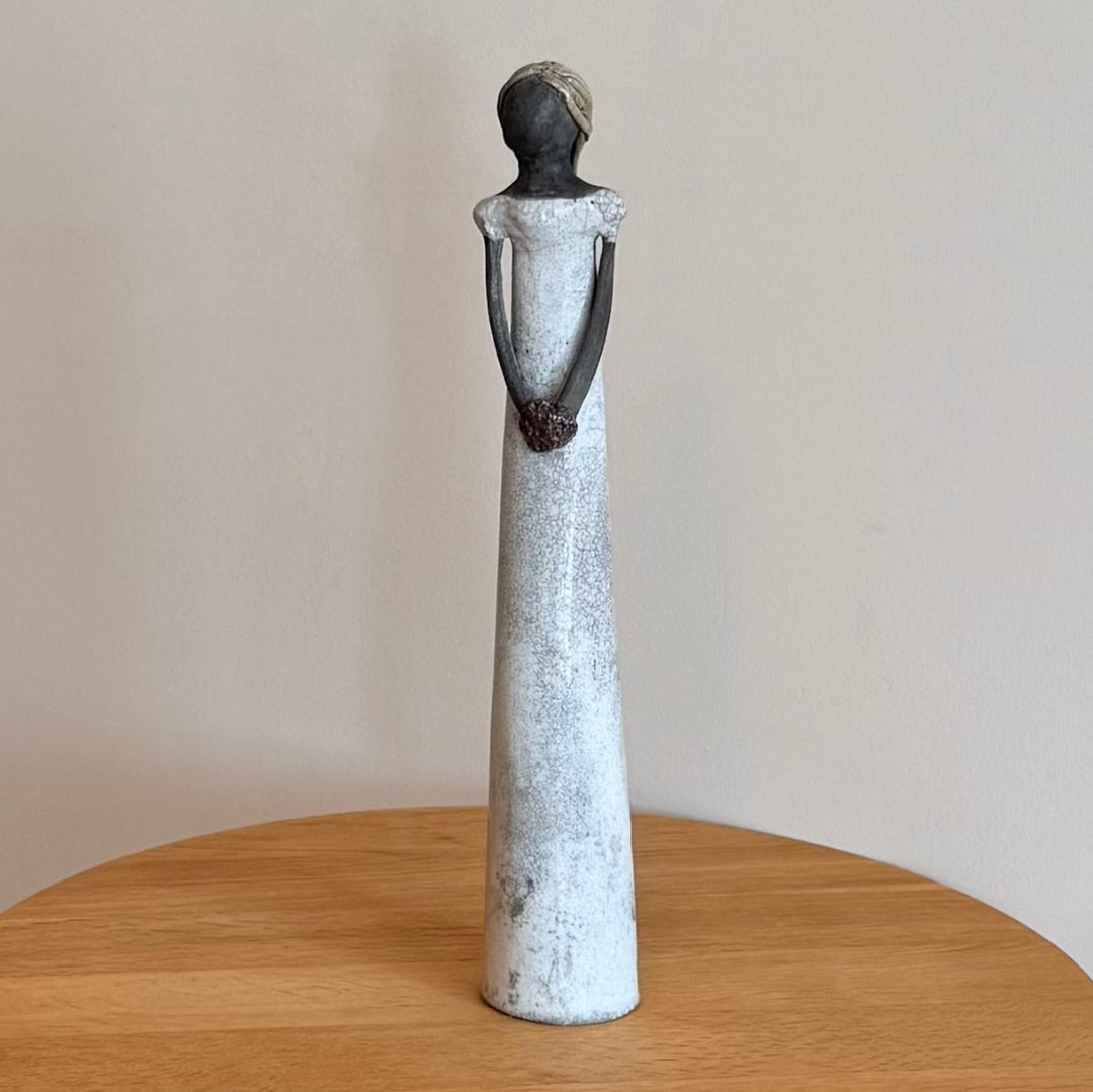 Ceramic sculpture of a standing figure on a wooden surface with a plain background