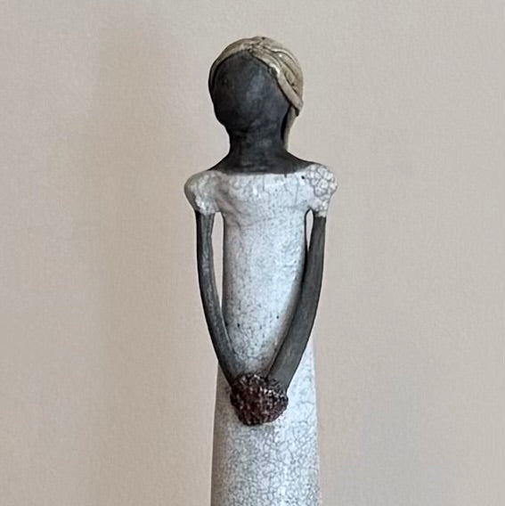 Close up view of a ceramic sculpture of a stylized figure on a plain background