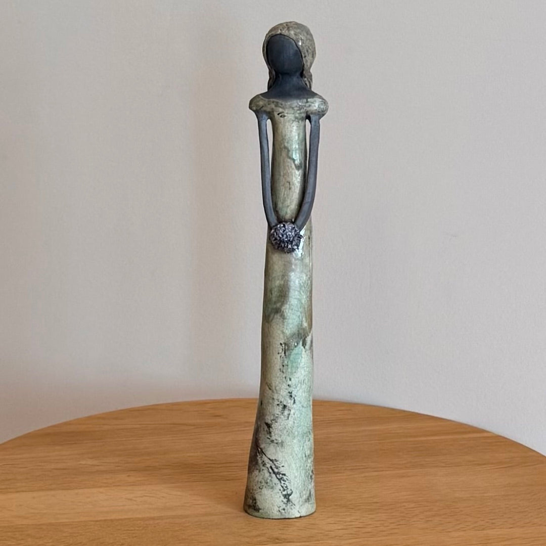 Ceramic of a standing figure on a wooden surface with a plain background