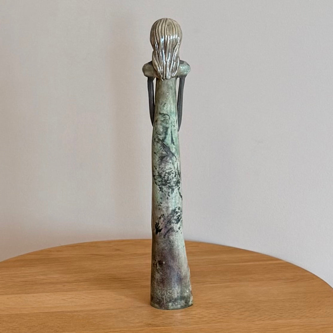 Ceramic sculpture of a figure on a wooden surface with a plain background