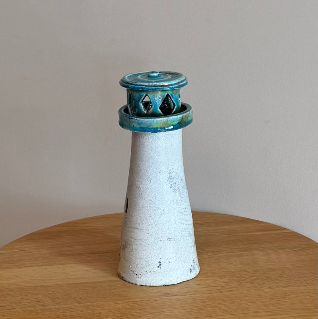 Ceramic lighthouse tealight holder sculpture on a wooden surface with a plain background