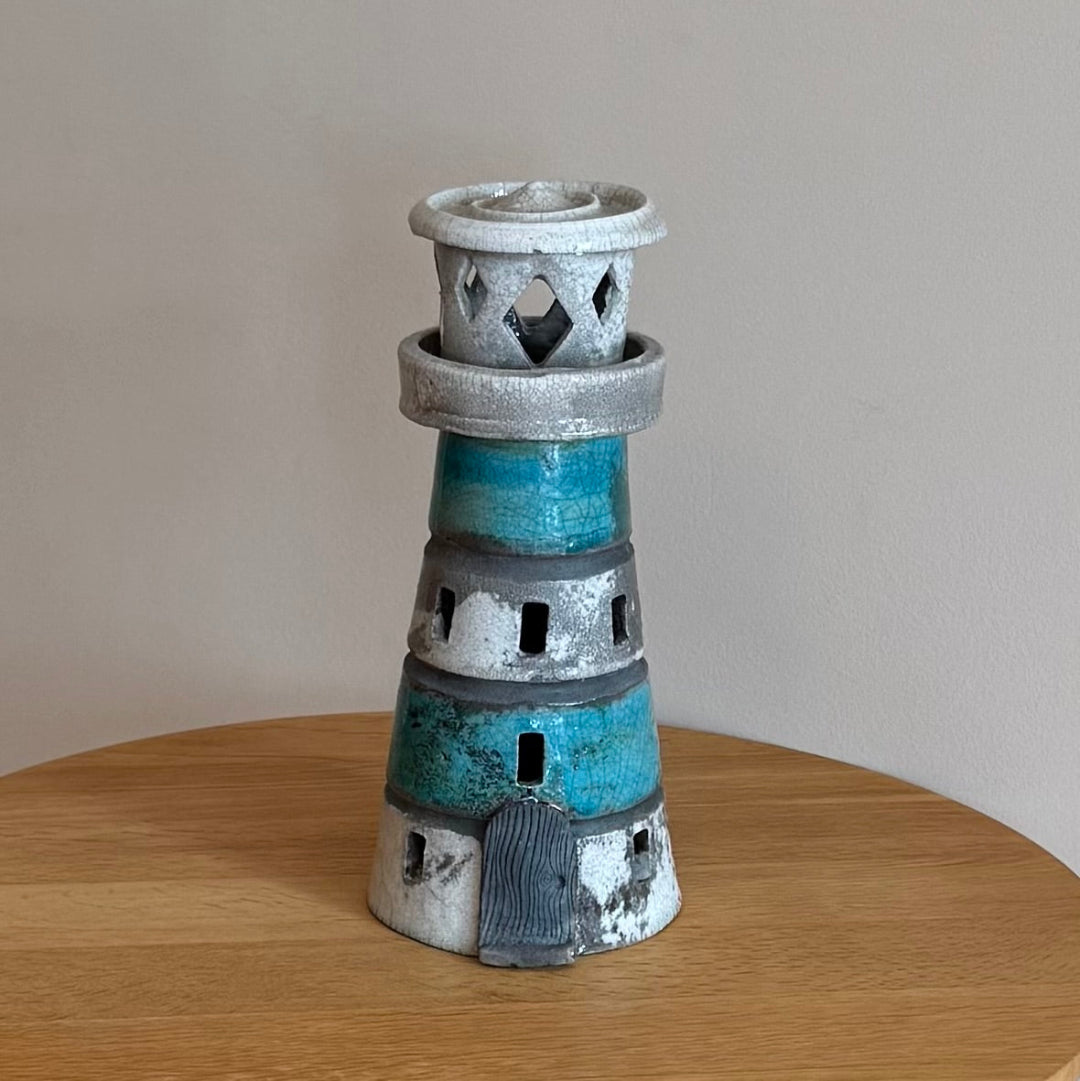 Ceramic lighthouse tealight holder sculpture on a wooden surface with a plain background