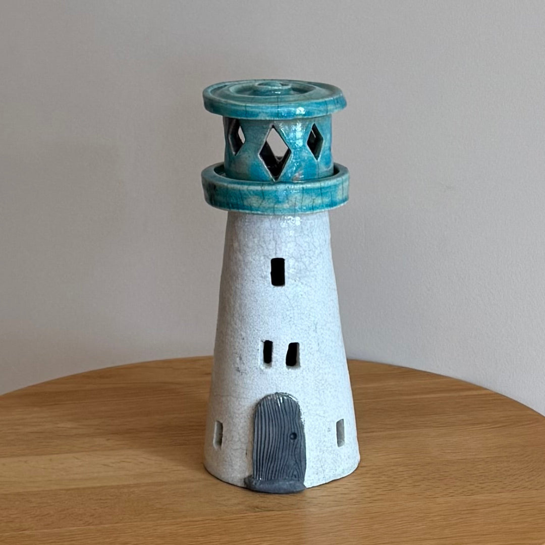 Ceramic lighthouse tealight holder sculpture on a wooden surface with a plain background