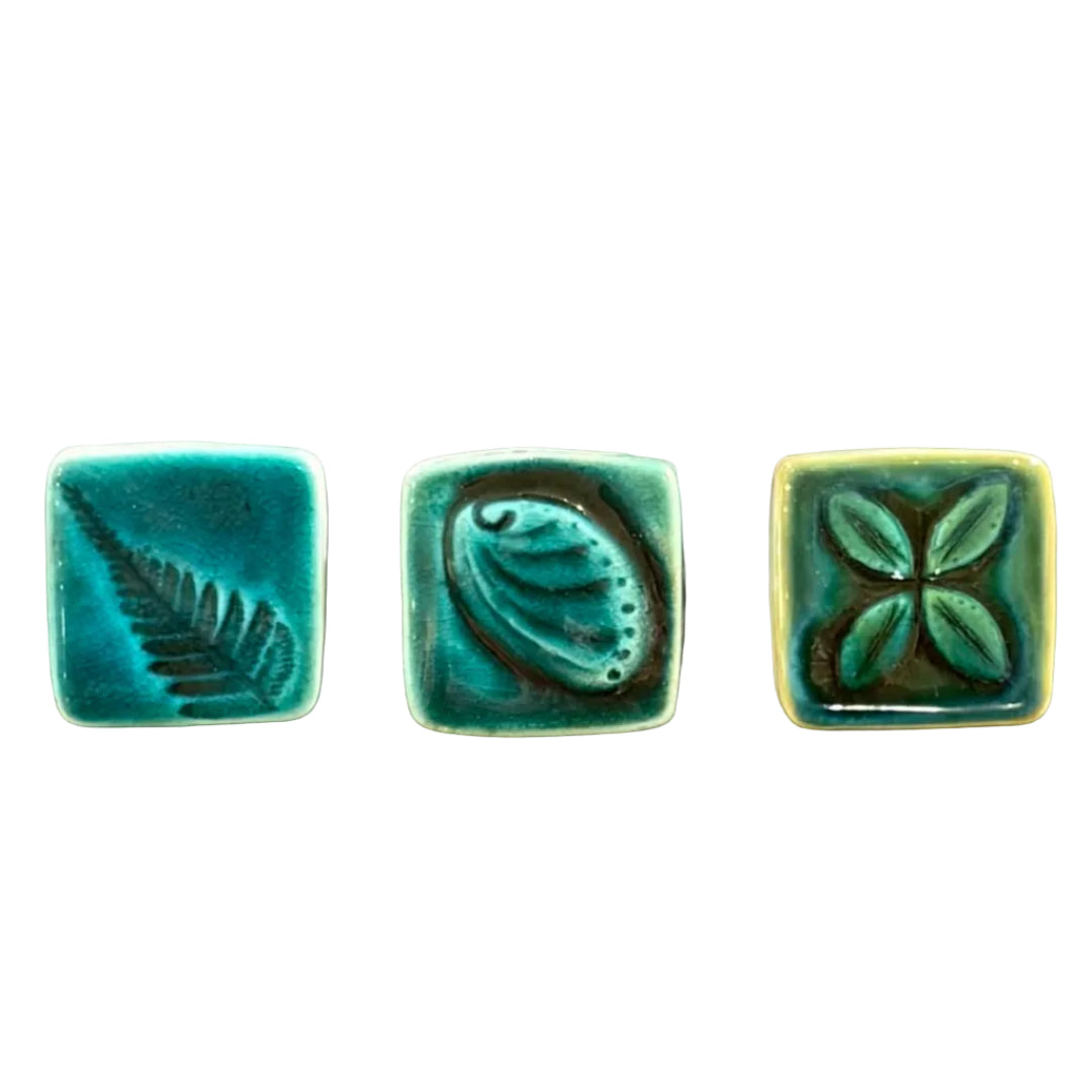 Three square ceramic tiles with leaf & shell designs on a white surface