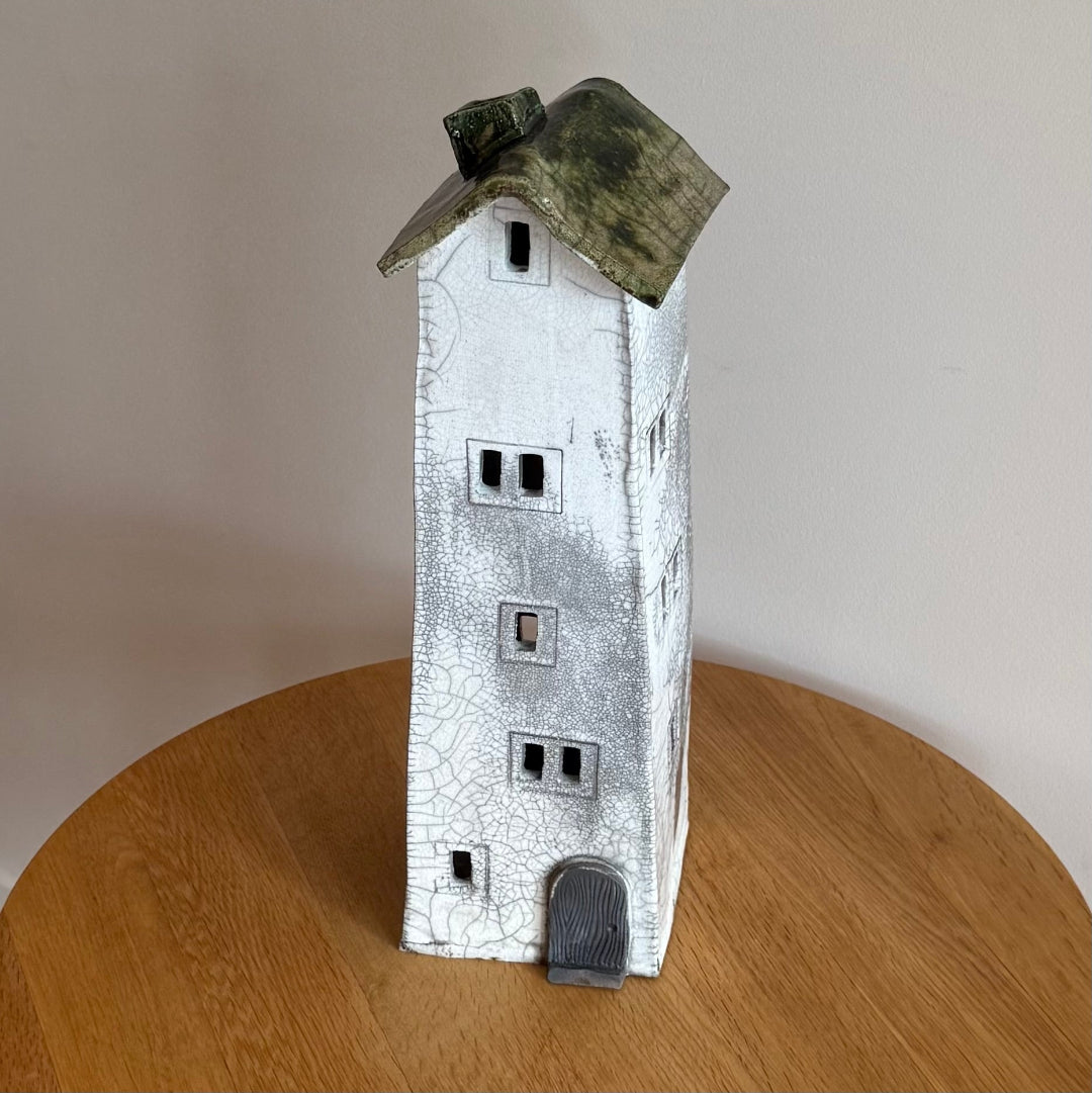 Ceramic tall house with a green roof & grey door on a wooden surface