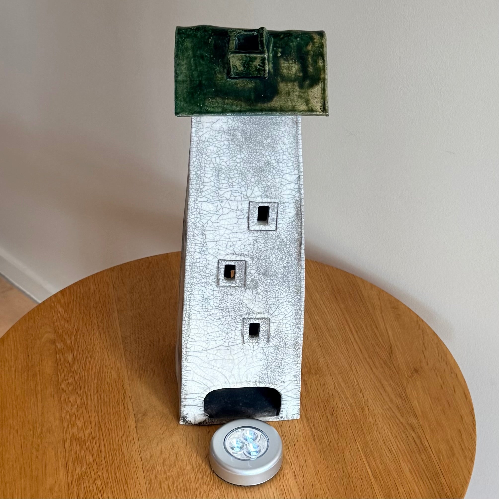 Ceramic tall house with a green roof on a wooden surface with battery light