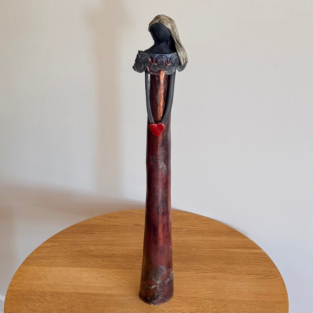 Ceramic figurine holding a red heart on a wooden table against a plain background
