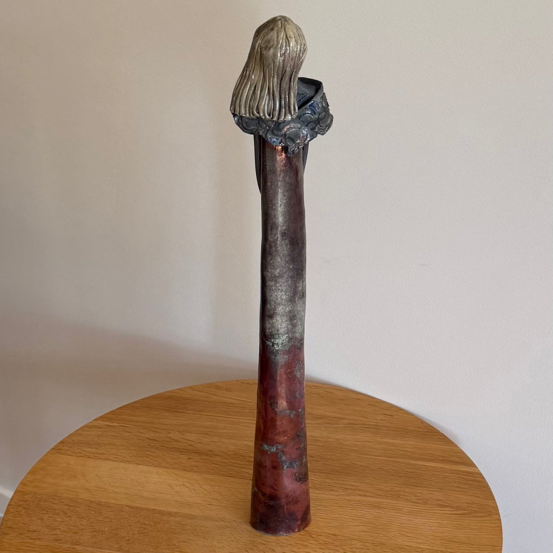 Back view of a ceramic copper-coloured figure on a wooden table.