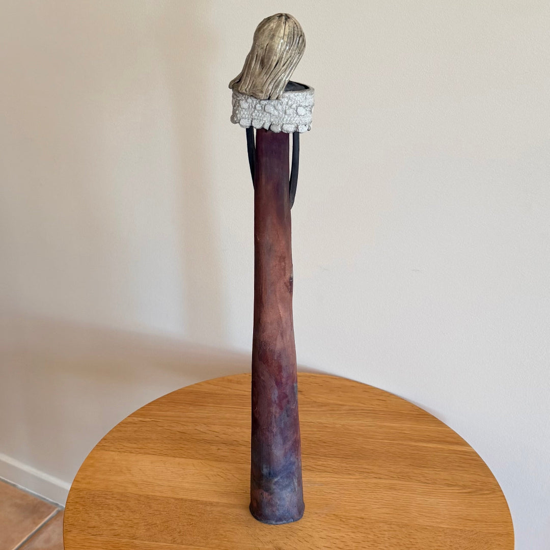 Back view of a ceramic figure on a round wooden table against a plain wall.