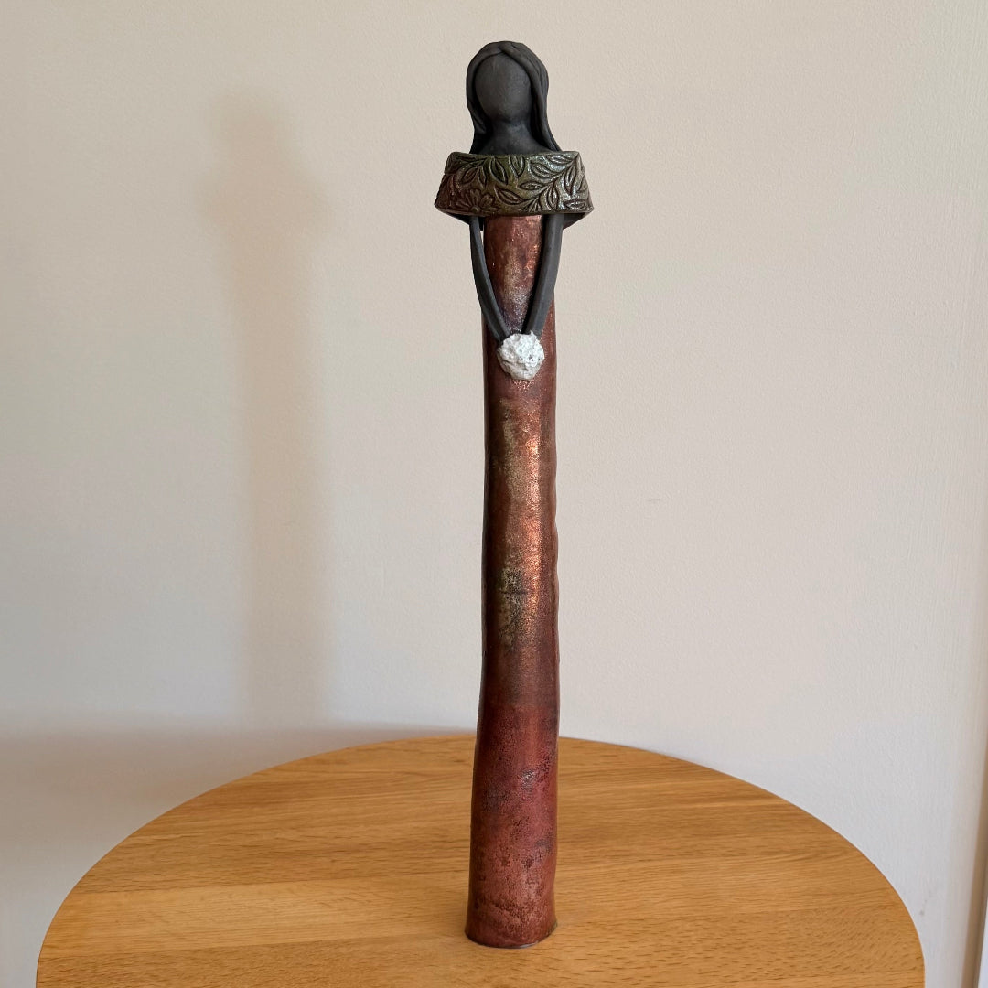 Ceramic figure with white posy and ornate collar on a round wooden table.