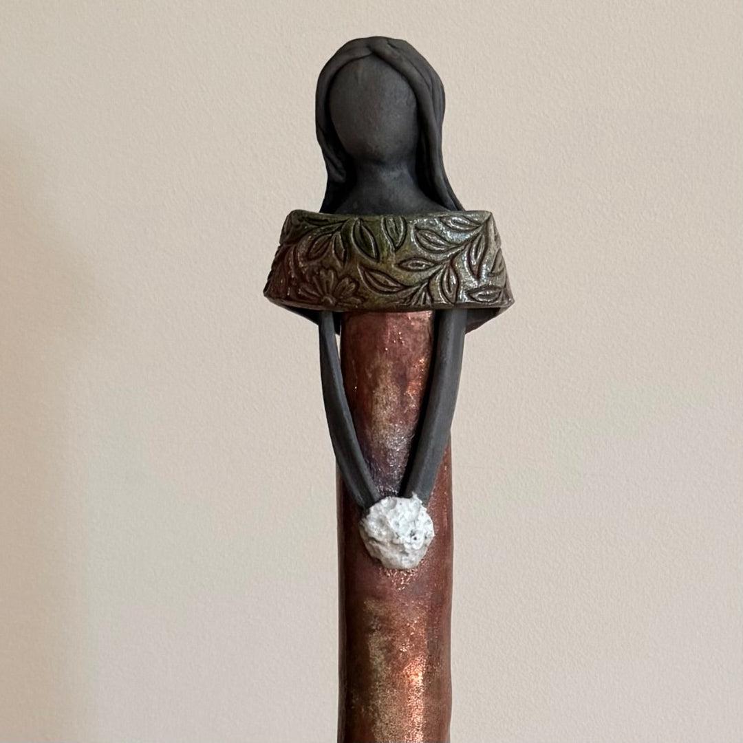 Close up view of a ceramic figure holding a white posy on a beige background