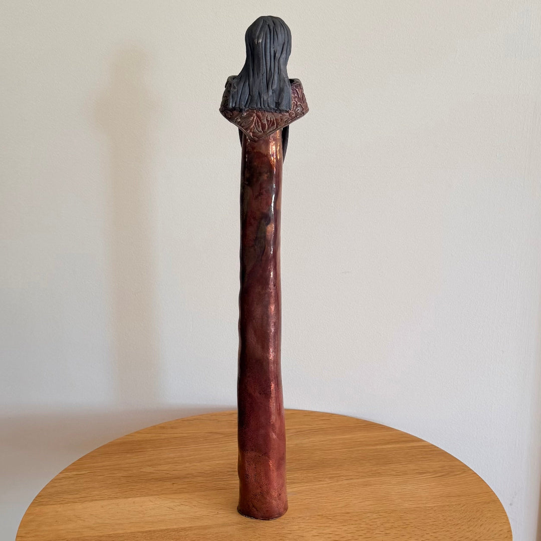 Back view of a ceramic figure on a light wooden surface.