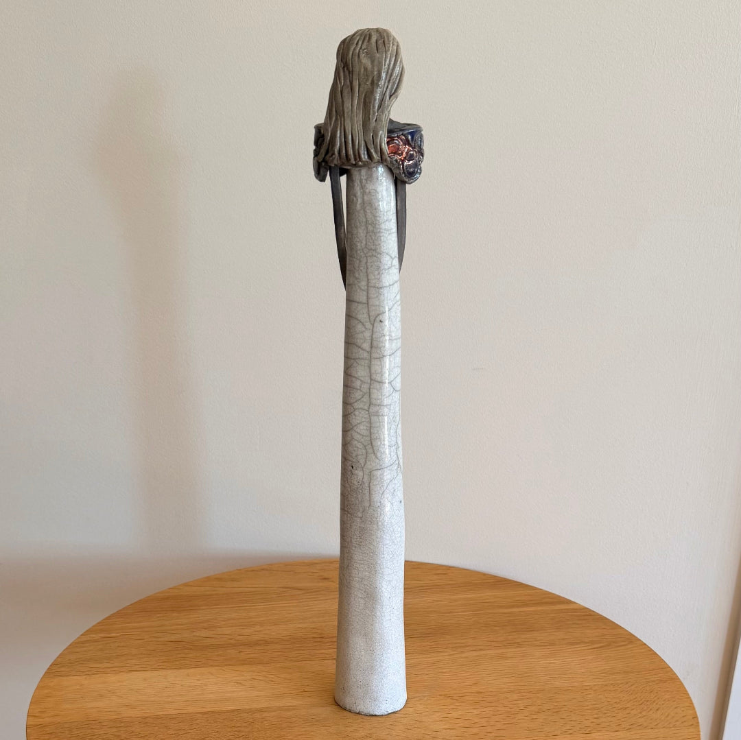 Back view of a ceramic lady with long hair on a wooden table against a plain wall.