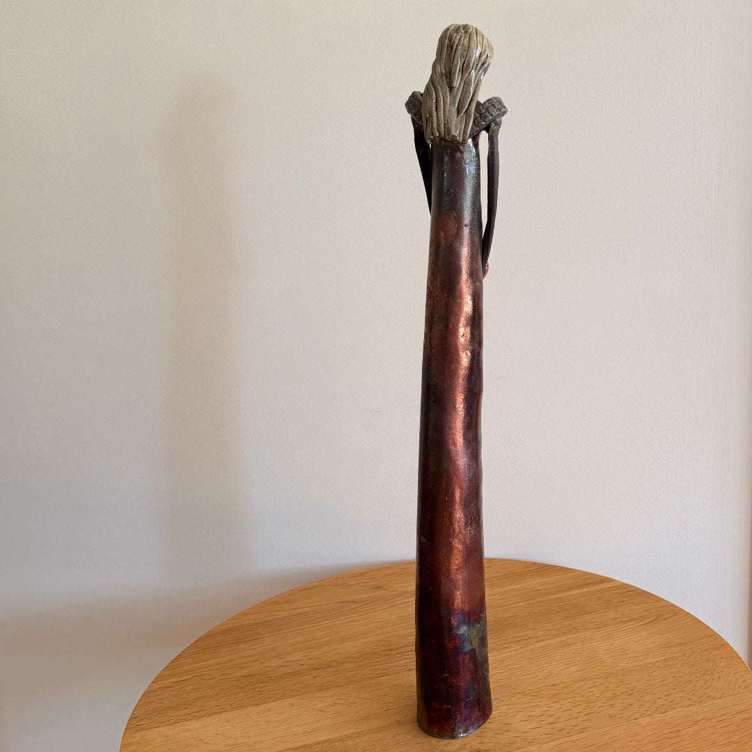 Back view of a ceramic sculpture of a figure placed on a wooden surface.