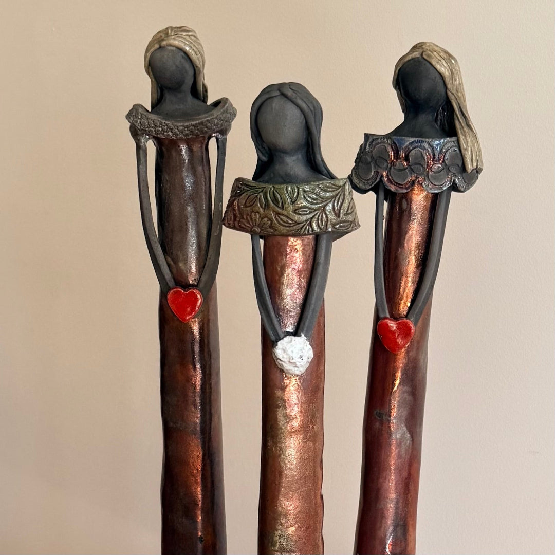 Close up view of three ceramic figures holding hearts & flowers on a beige background