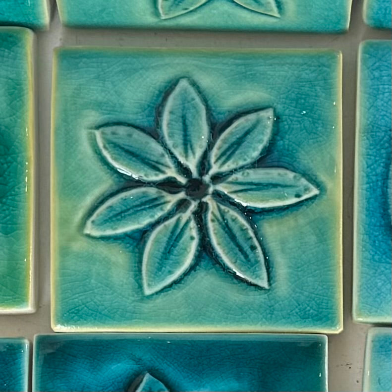 Close-up of a teal ceramic tile with a floral design