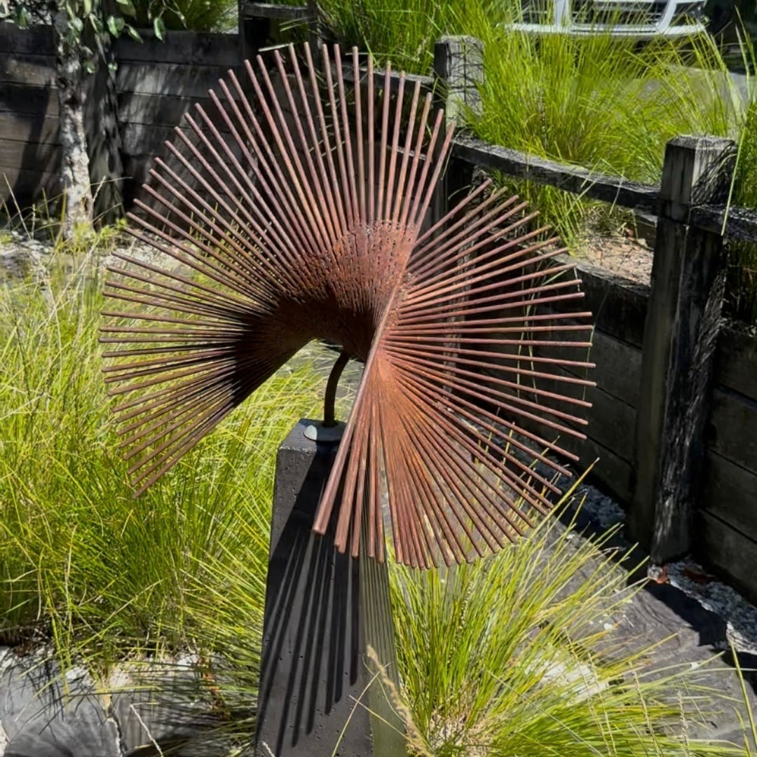 Decorative metal sculpture with fan-like design in a garden setting
