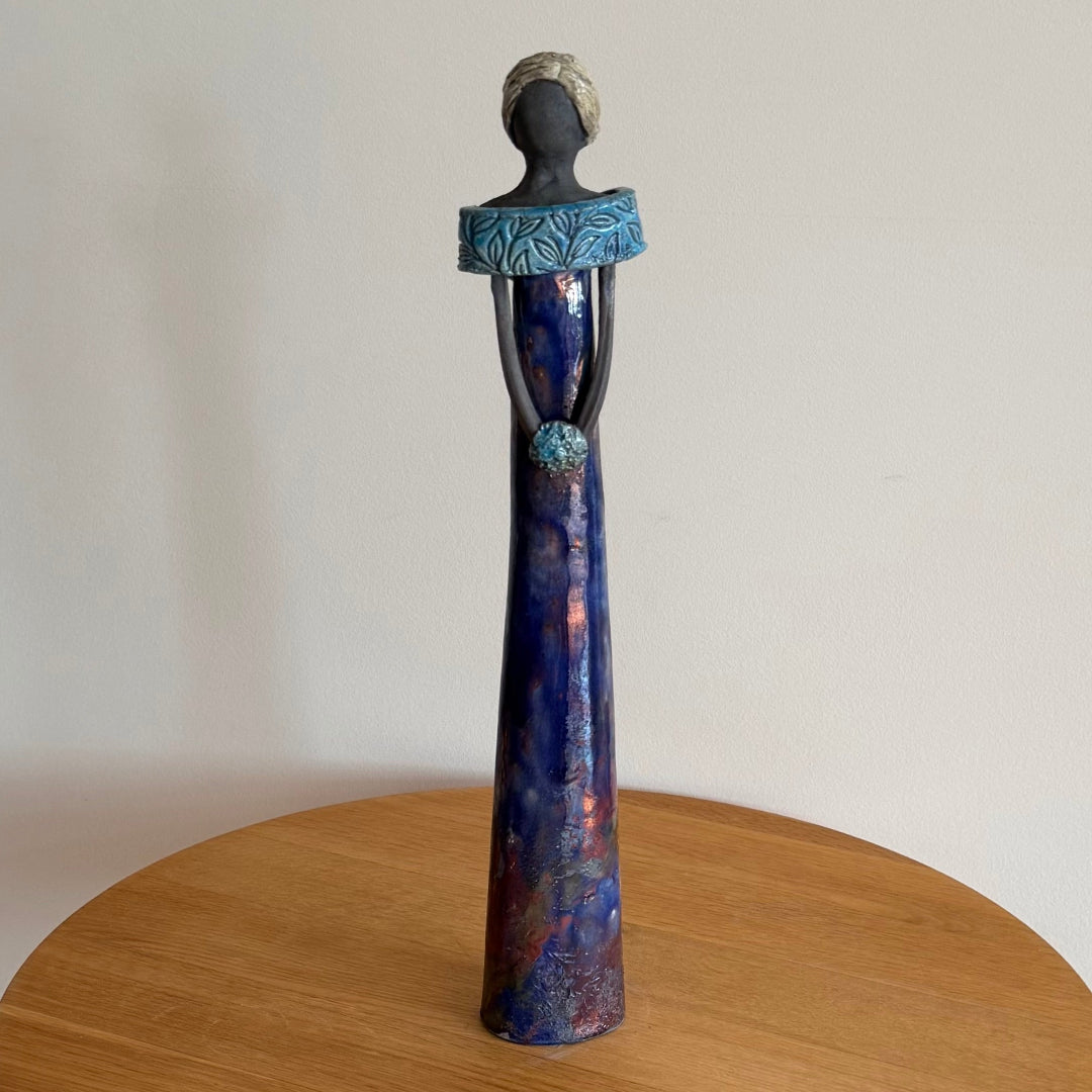 Ceramic tall lady holding a posy with blue glazed dress on a wooden surface