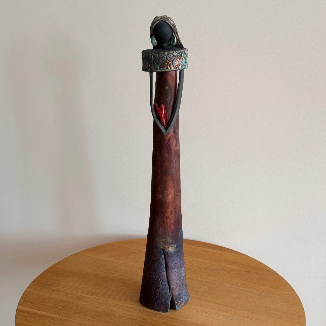Ceramic woman with matt glaze dress & red heart ona wooden surface against a plain background