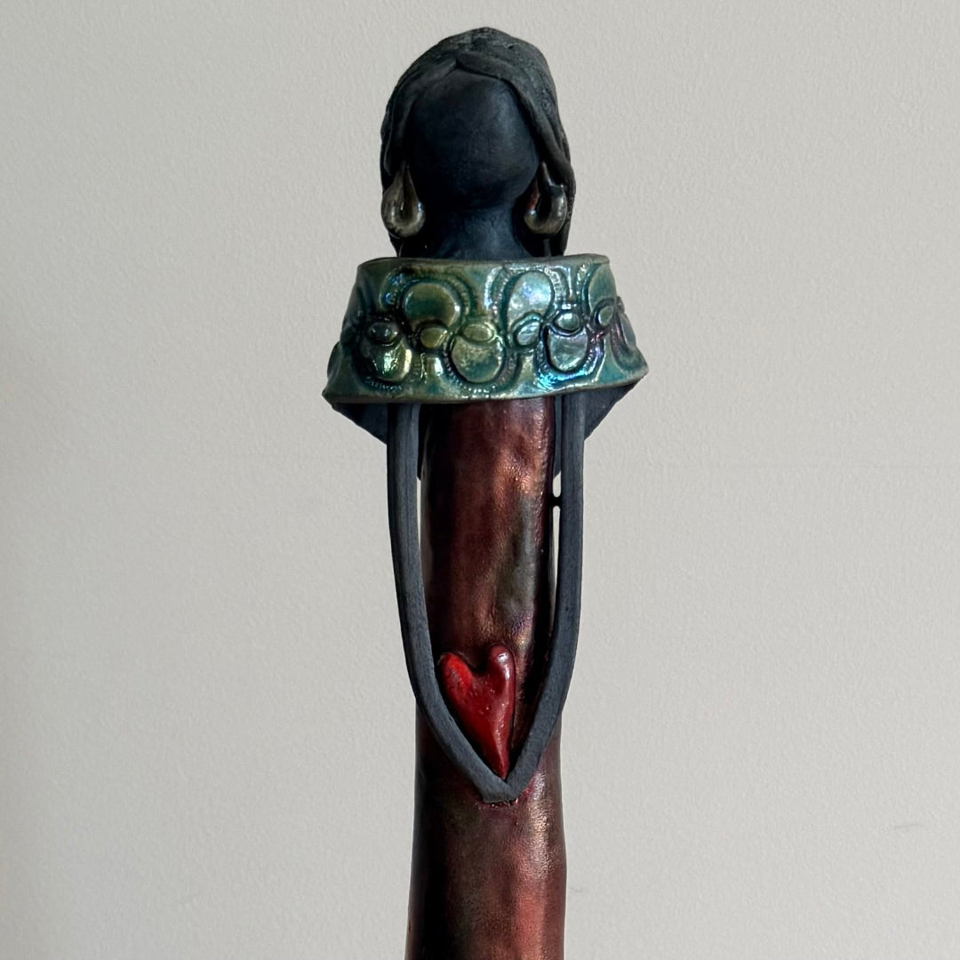 Half view of a ceramic woman with green earrings & collar on a beie background