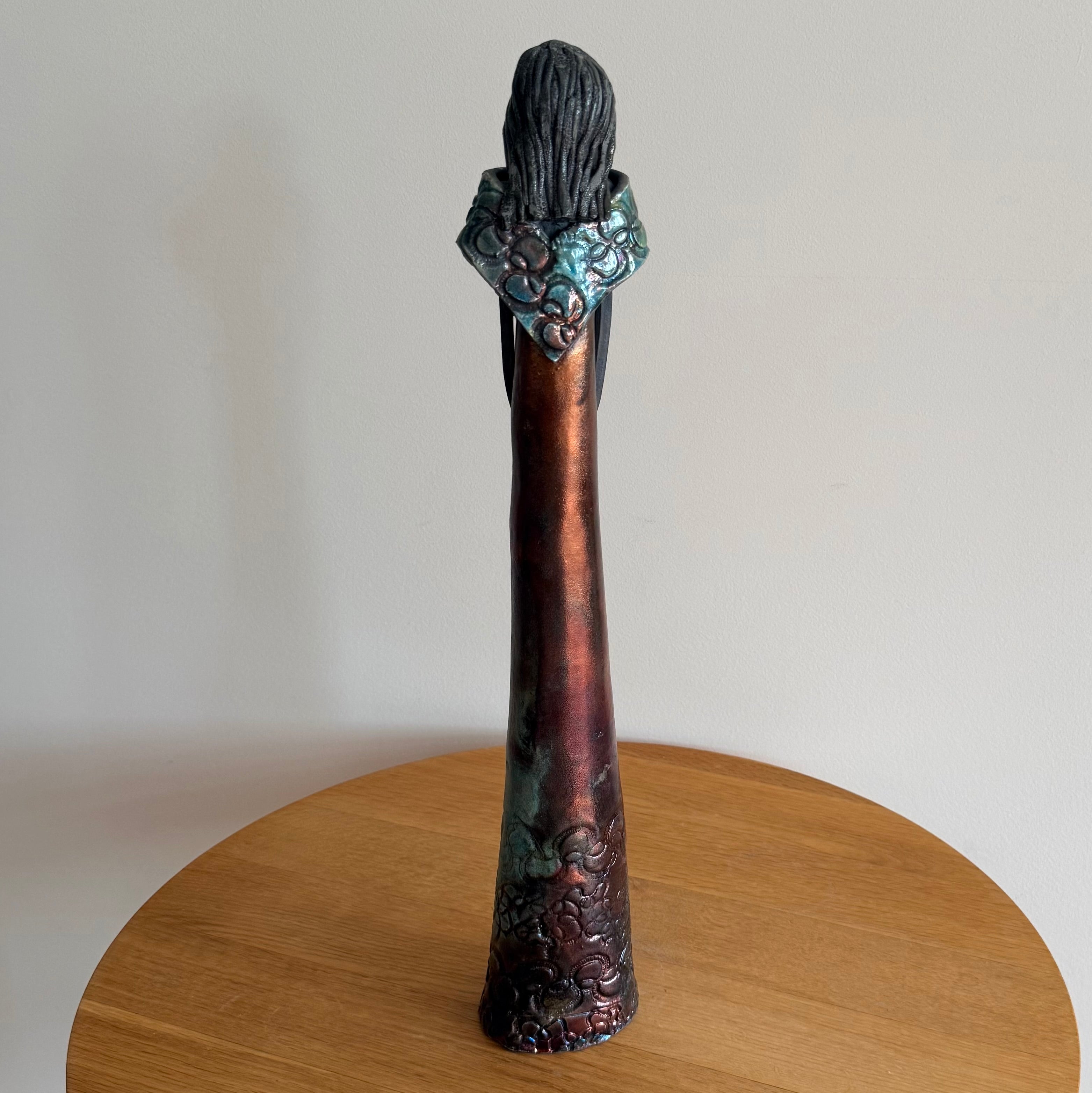 Back view of a ceramic woman on a wooden stand against a plain background