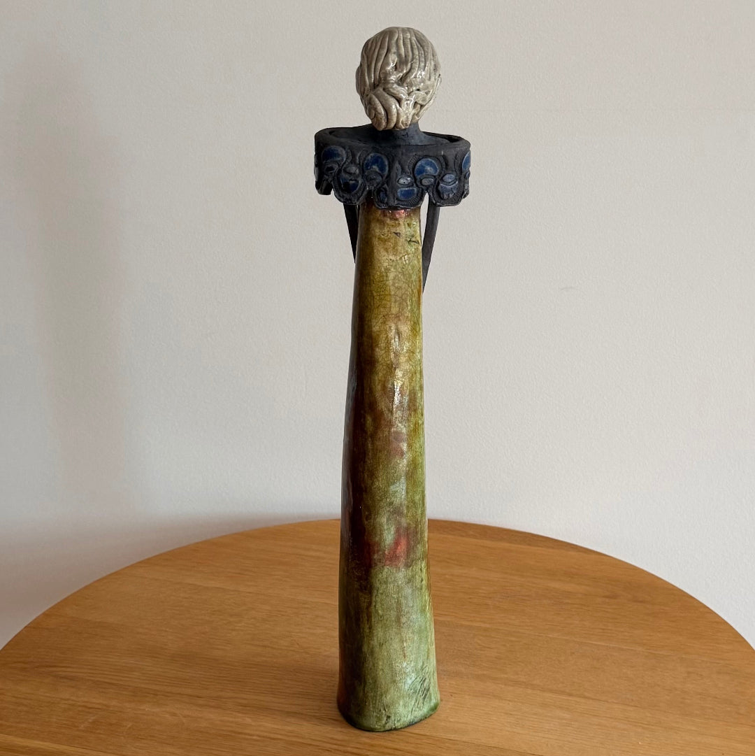 Tall ceramic woman in a long dress with wide collar holding a blue posy on a wooden surface