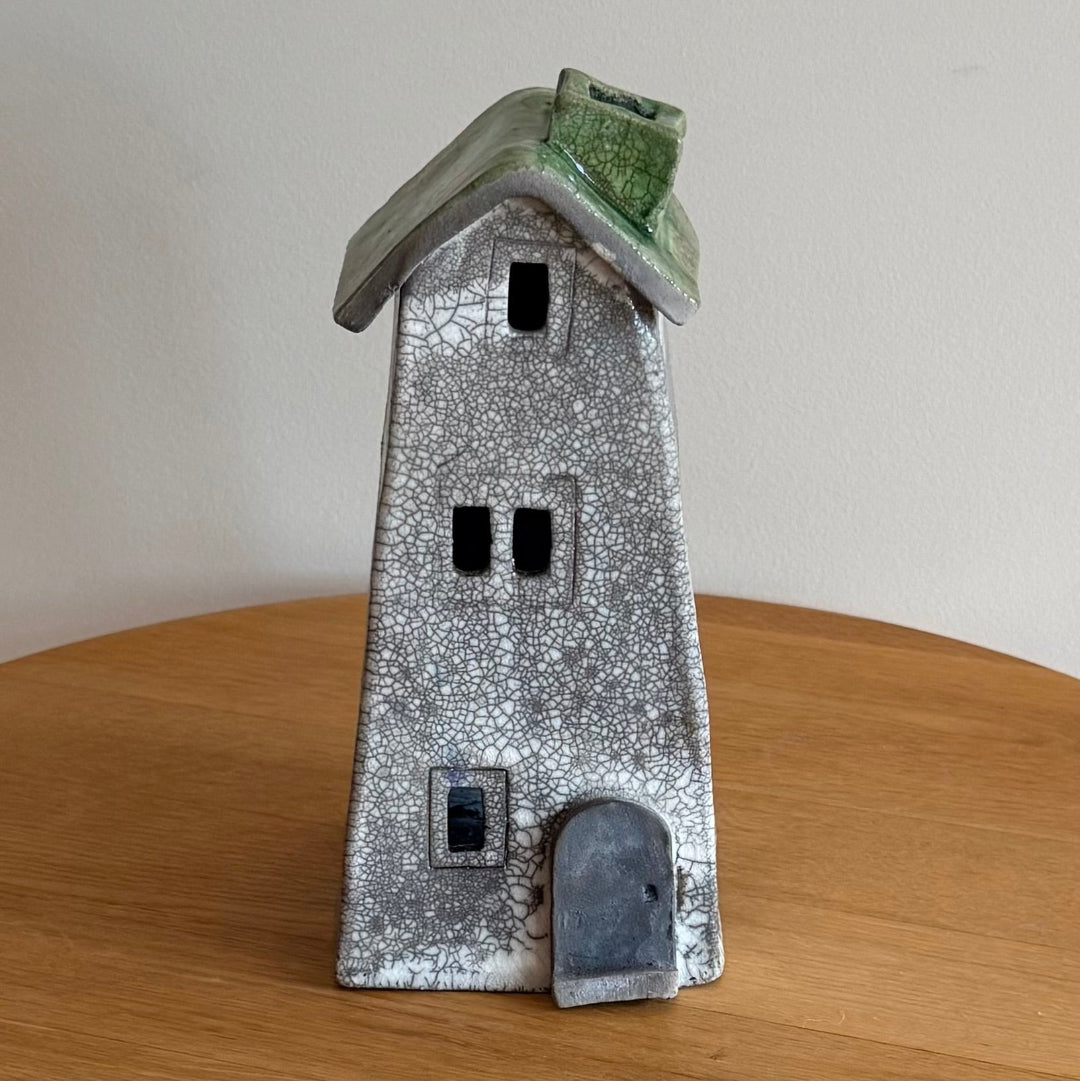 Ceramic tall house with textured surface and green roof on a wooden surface