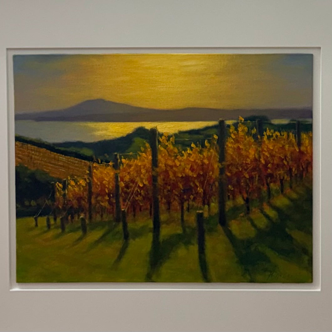 Framed painting of a vineyard with trees and a body of water in the background.