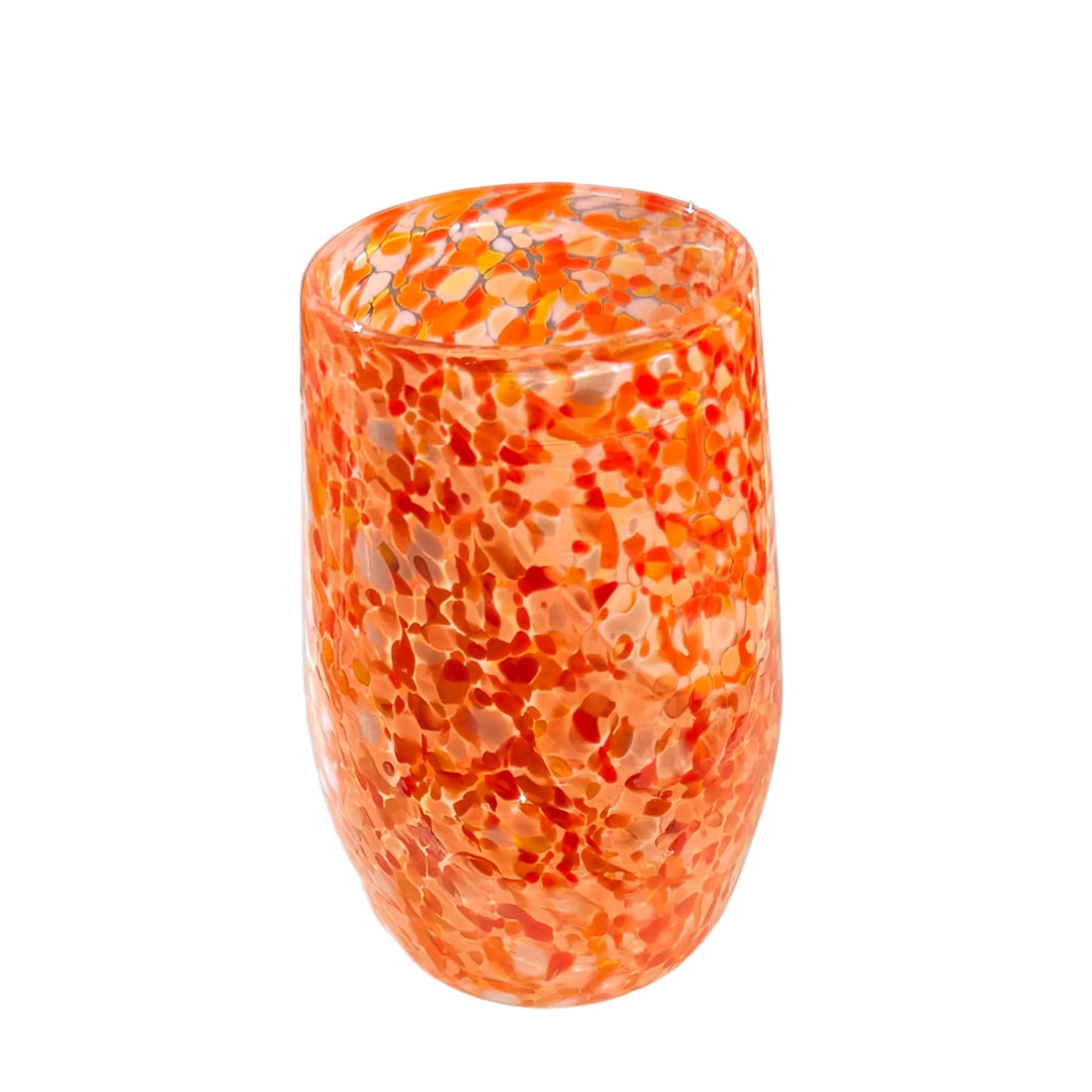 Orange and white speckled glass tumble on a white surface