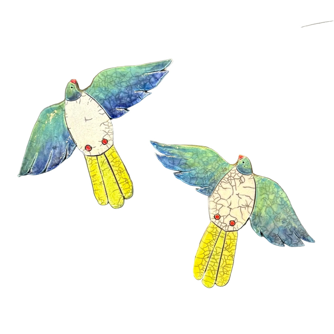 Two colourful ceramic Kereru flying shaped wall tiles on a white background