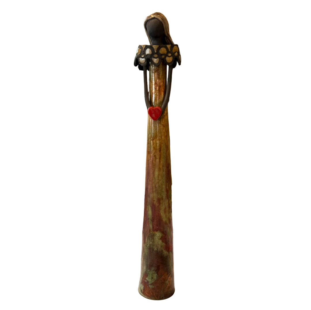 Tall, decorative ceramic lady with a yellow glaze holding a red heart on a white background