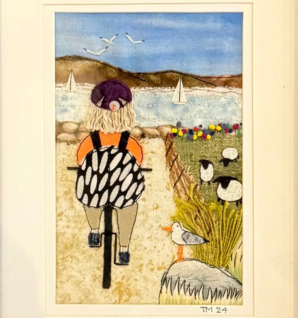 Framed artwork of a person on a bike on a path by the beach.