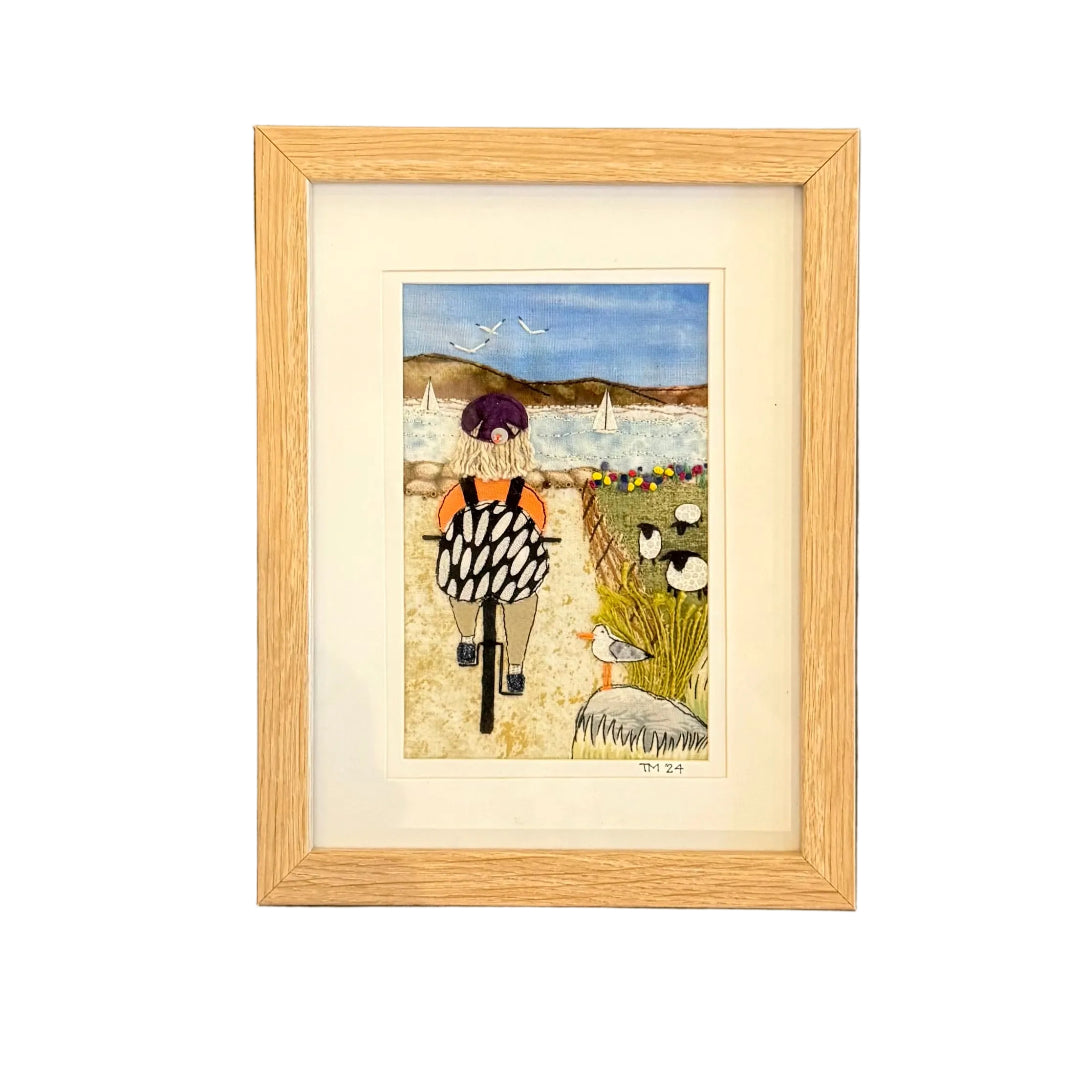 Framed artwork of a person on a bike on a path by the beach