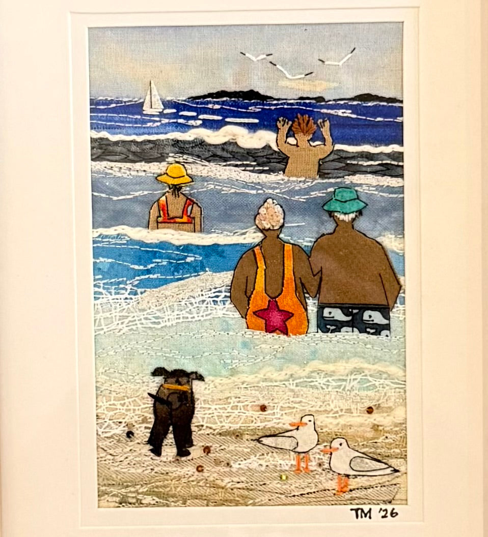 Textile artwork of two people and a dog at the beach with seagulls.