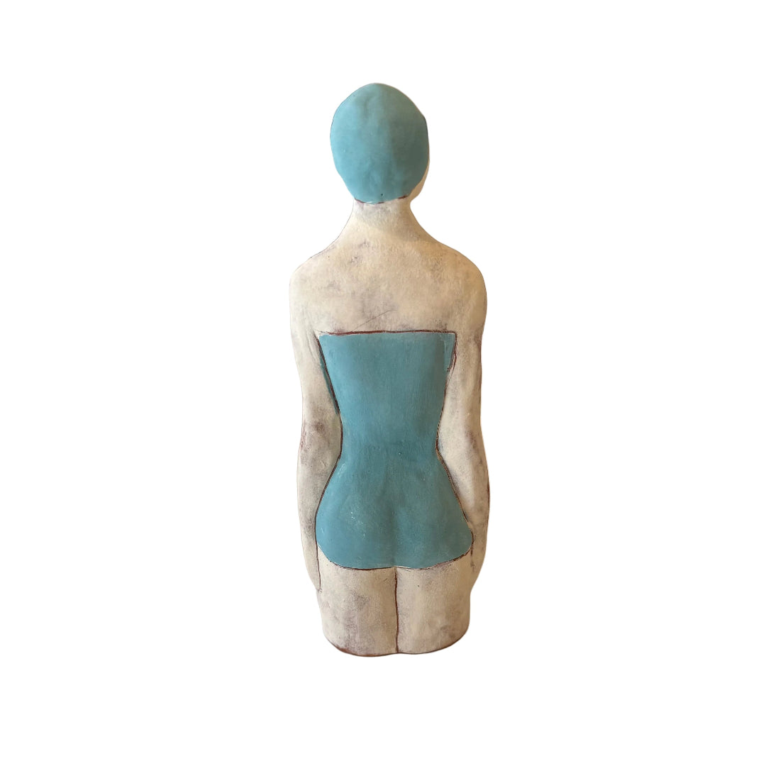 Back view of a ceramic sculpture of a Swimmer in blue swimsuit & cap on a white background