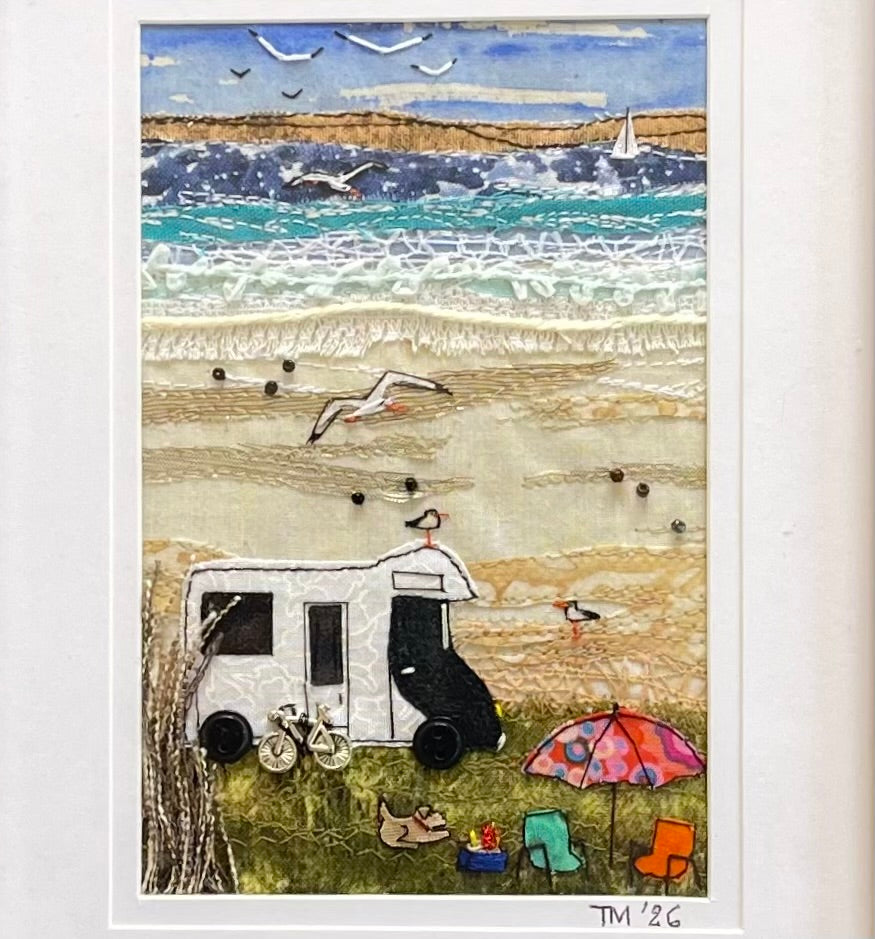A textured mixed-media beach scene artwork featuring a white caravan, silver bicycle, beach umbrella, chairs, seagulls, waves, and a blue sky, presented on a white mat background.