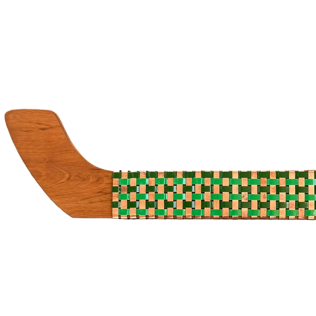 Cose up of a wooden wall Waka with woven copper, green and black aluminium pattern on a white background