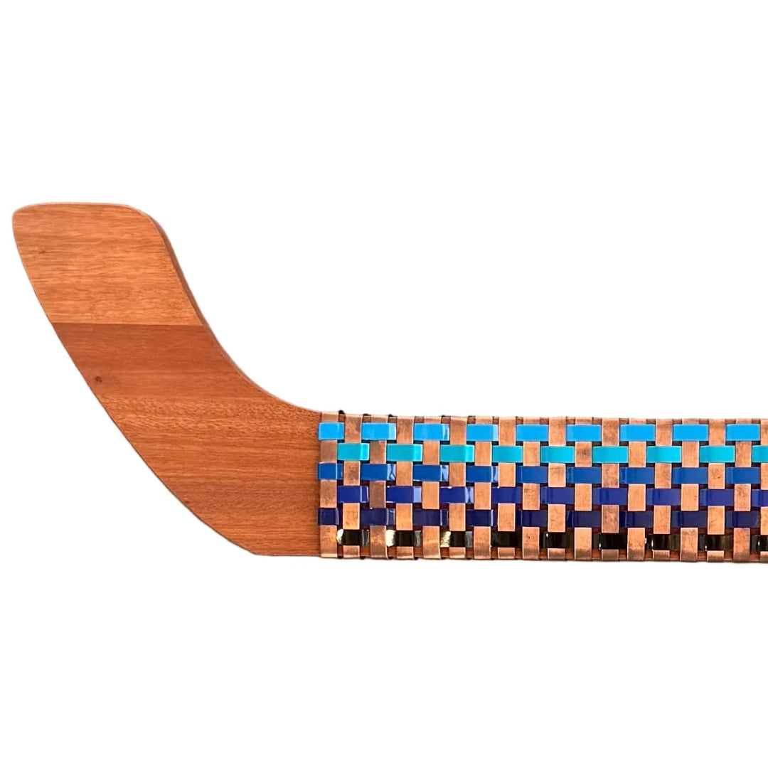 Cose up of a wooden wall Waka with woven copper, blue and black aluminium pattern on a white background