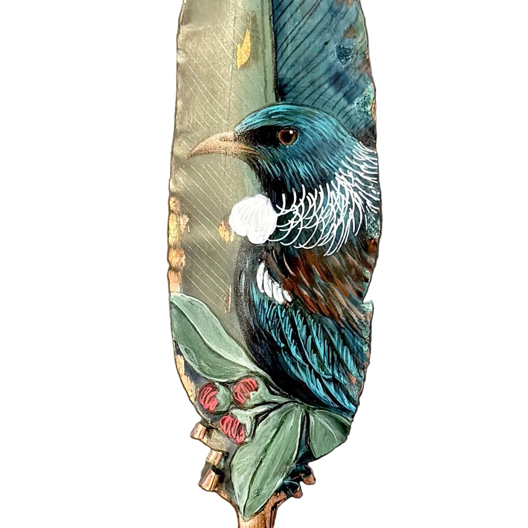 Close up view of a decorative copper feather with a painted Tui bird on a white background