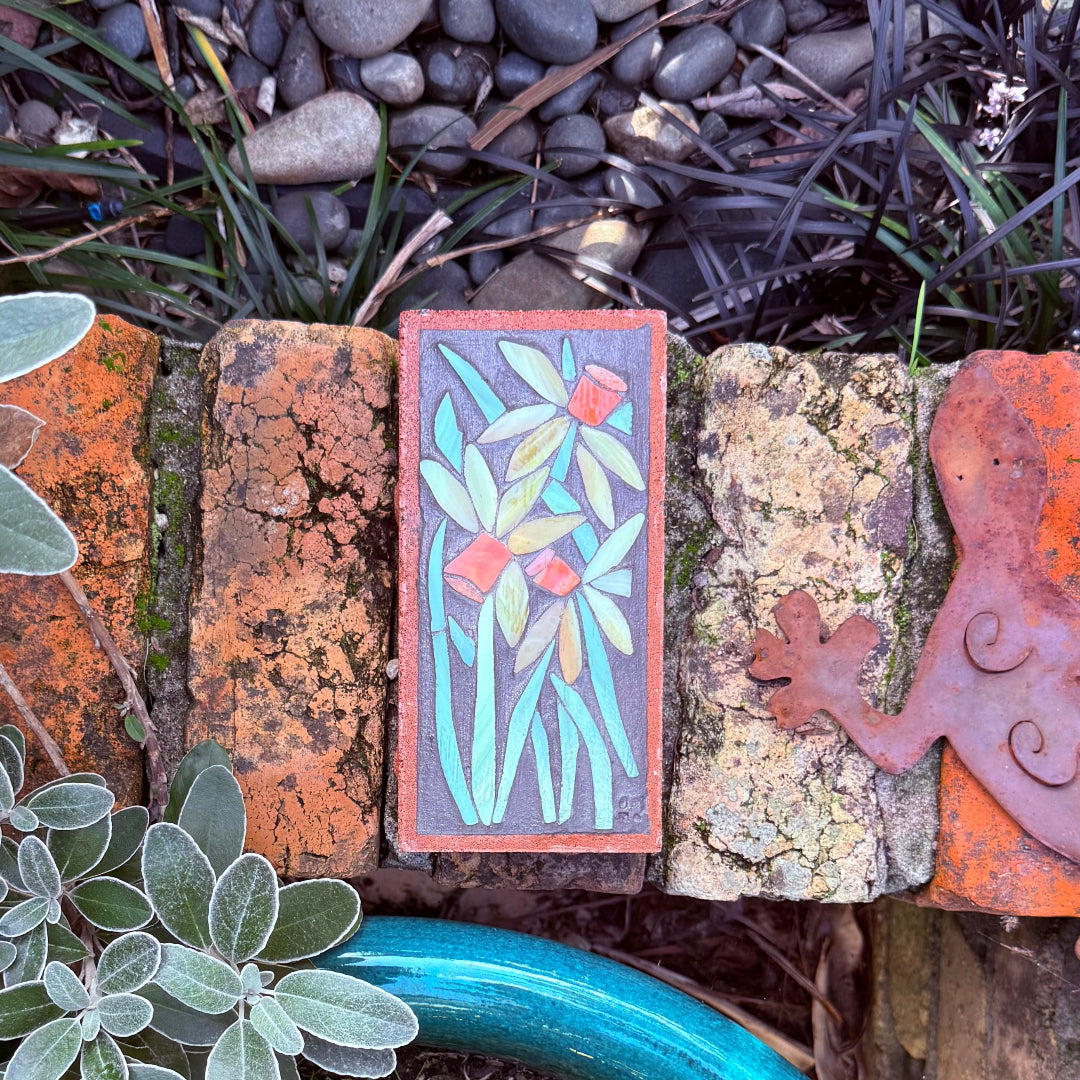 Decorative mosaic brick with floral design on a brick wall surrounded by plants