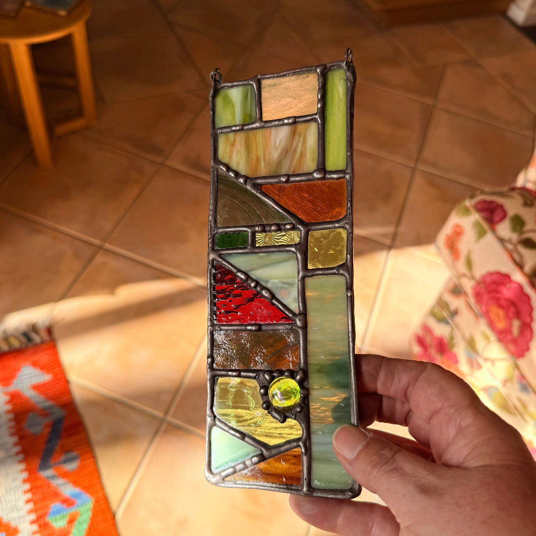 Hand holding a stained glass panel with geometric design above a tiled floor.
