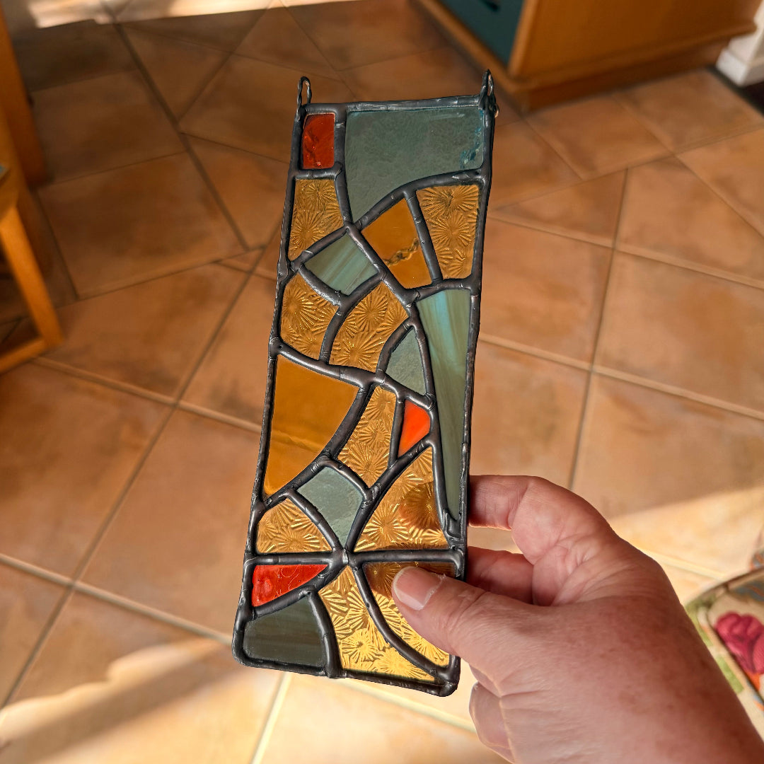 Hand holding a stained glass panel with geometric pattern above a tiled floor background