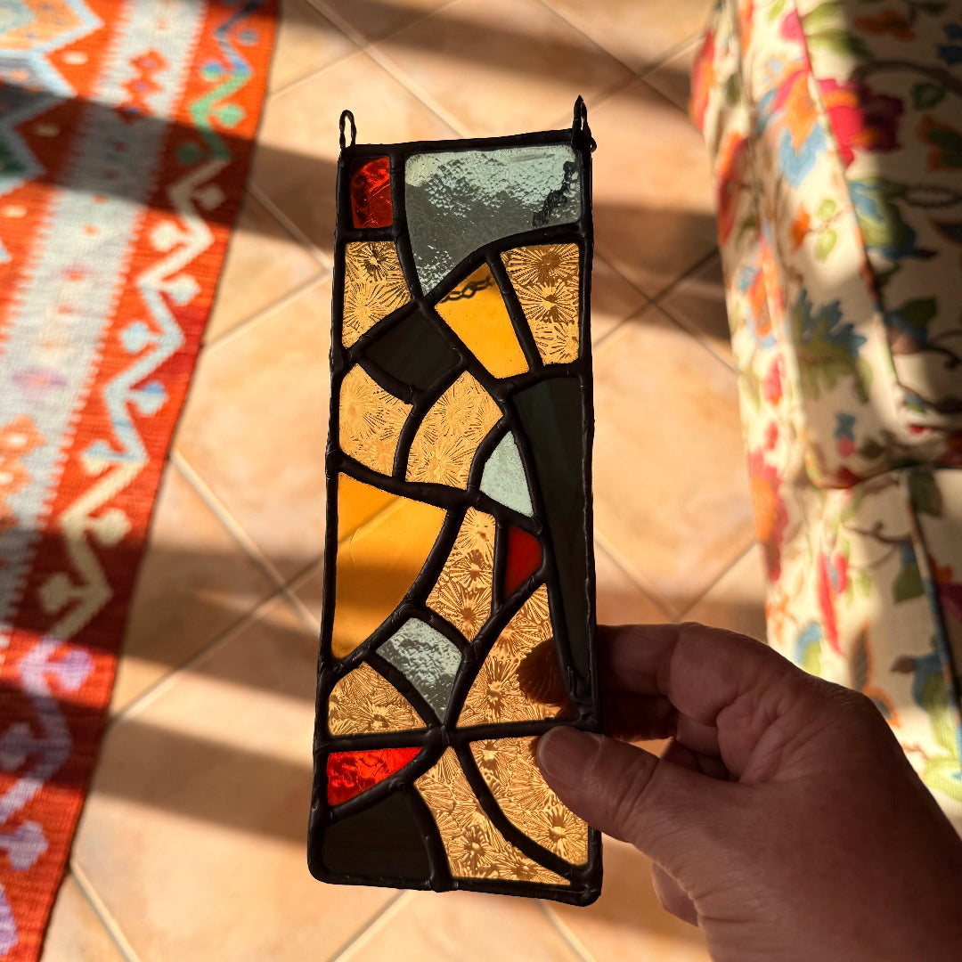 Hand holding a stained glass panel with geometric pattern above a tiled floor.