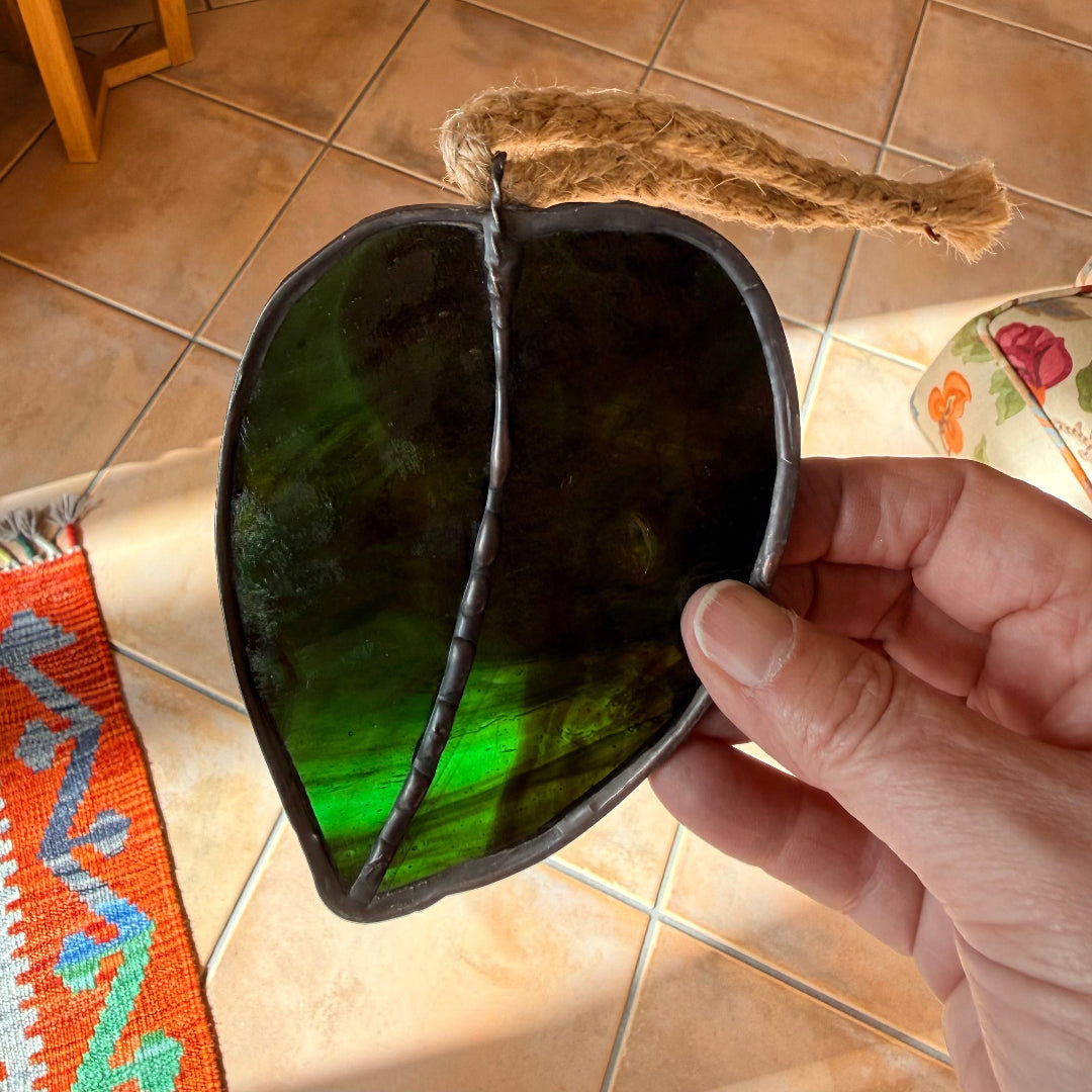 Hand holding a glass kawakawa wall hanging above a tiled floor.