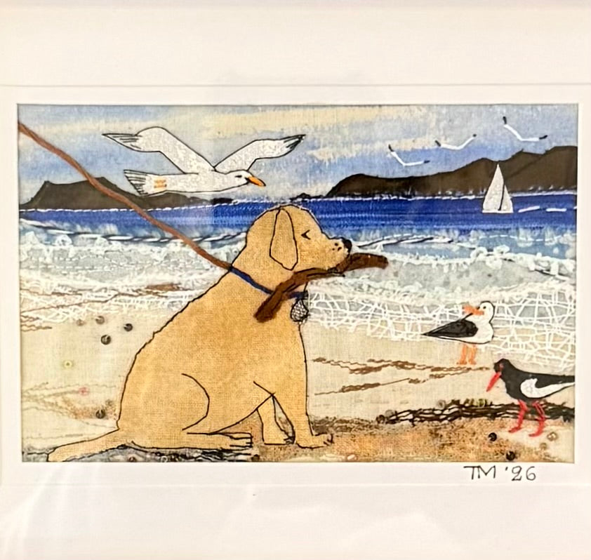 Textile artwork of a dog on a leash with seagulls and a sailboat in the background