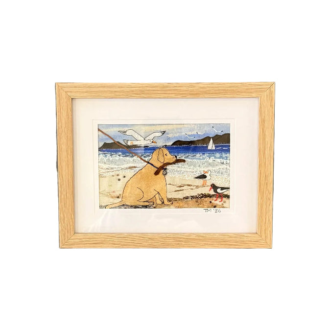 Framed textile artwork of a dog on a beach against a white wall