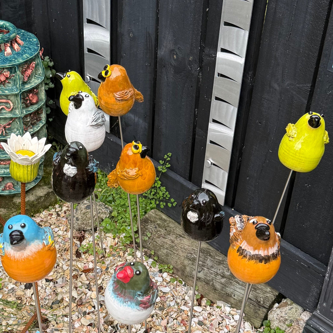 Colorful bird-shaped garden stakes in front of a black wooden fence.