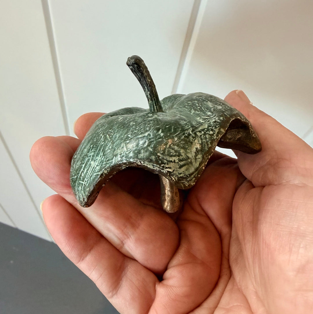 Hand holding a greenish cast bronze half eaten apple against a white background