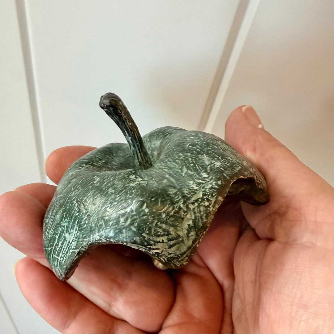 Hand holding a greenish cast bronze half eaten apple against a white background